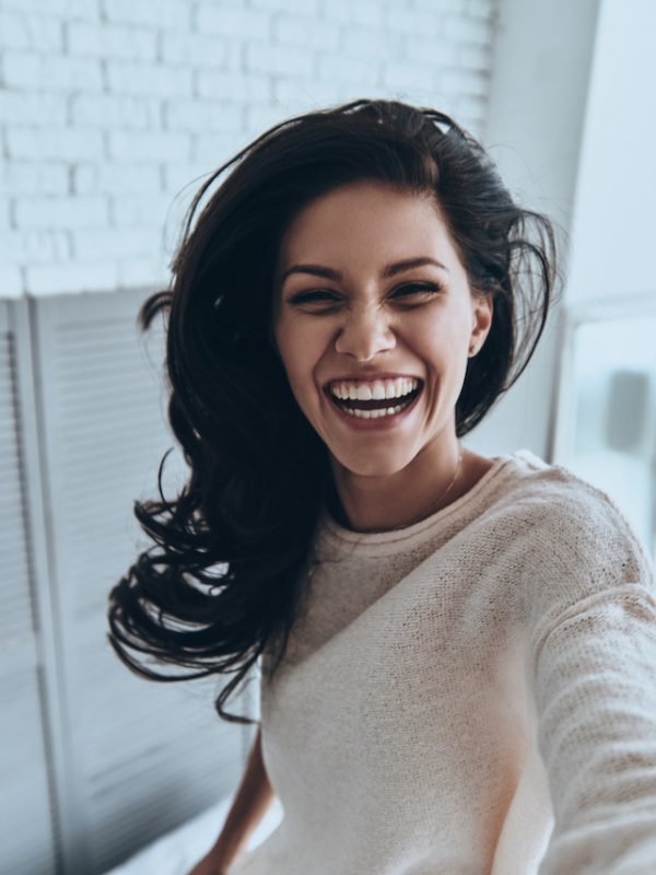 Sincere smile. Self portrait of attractive young woman looking at camera and smiling while standing in the bedroom at home